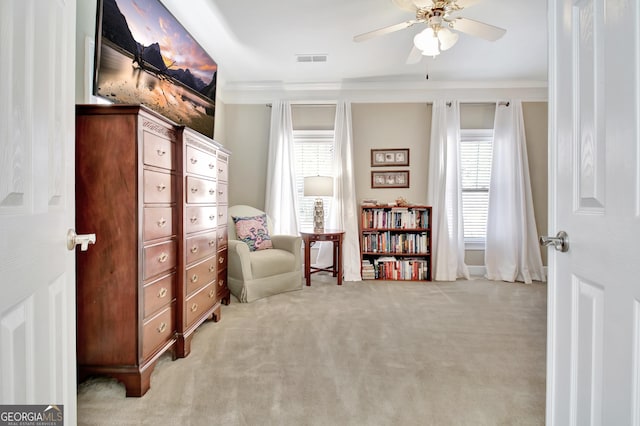 interior space with ceiling fan, visible vents, light colored carpet, and ornamental molding