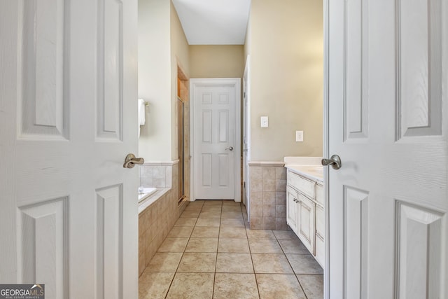 full bath featuring a shower with door, tile walls, tiled bath, vanity, and tile patterned flooring