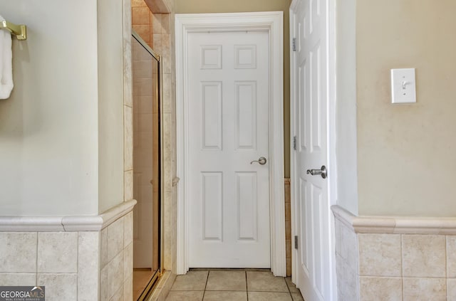 corridor with light tile patterned floors, tile walls, and wainscoting