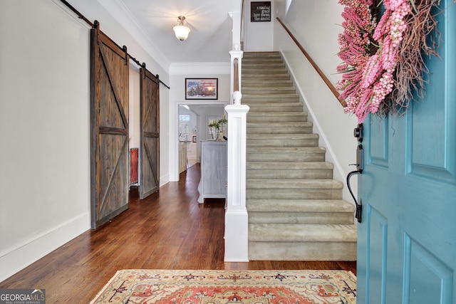 entrance foyer with a barn door, baseboards, wood finished floors, stairs, and crown molding