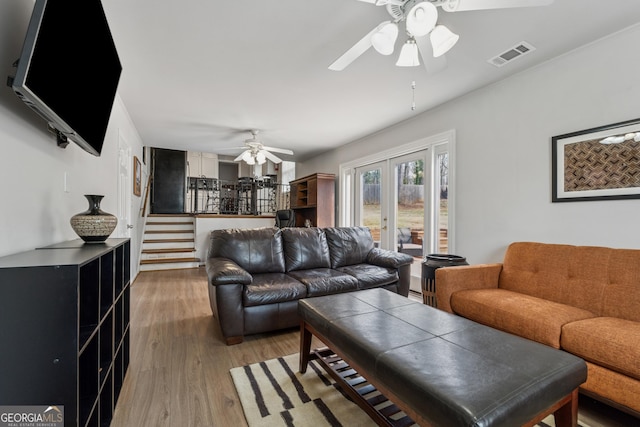 living room with visible vents, wood finished floors, a ceiling fan, and stairway