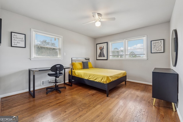 bedroom featuring visible vents, multiple windows, baseboards, and wood finished floors