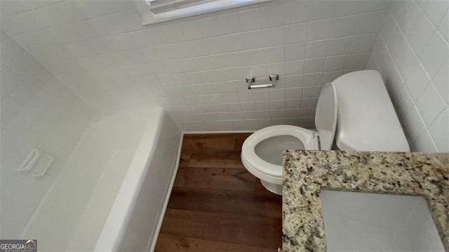 bathroom with a bathing tub, tile walls, toilet, and wood finished floors