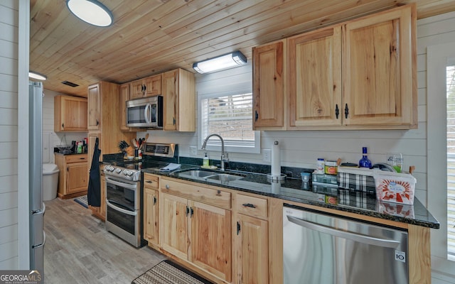 kitchen with stainless steel appliances, a sink, wood ceiling, light wood finished floors, and dark stone countertops