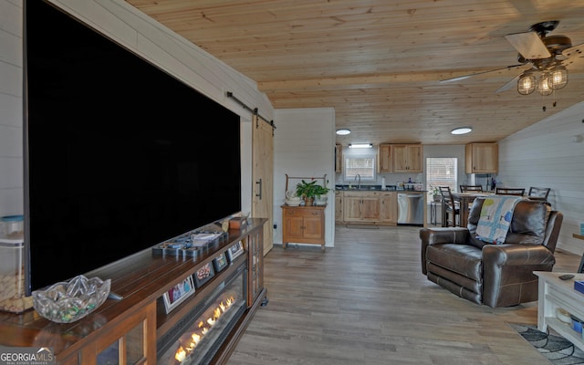 living area with ceiling fan, lofted ceiling, a barn door, light wood-style flooring, and wood ceiling