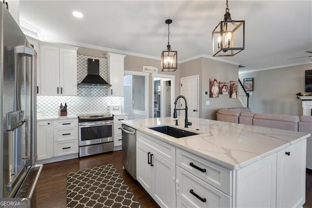 kitchen with stainless steel appliances, a sink, white cabinets, open floor plan, and wall chimney range hood