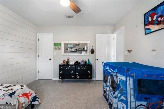 carpeted bedroom with a ceiling fan, visible vents, and wood walls