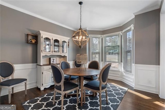 dining space featuring ornamental molding, dark wood-style flooring, wainscoting, and an inviting chandelier