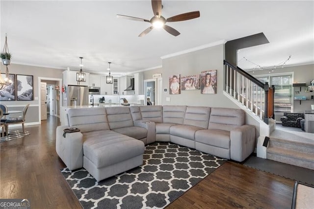 living room featuring ceiling fan with notable chandelier, stairway, dark wood-style flooring, and ornamental molding