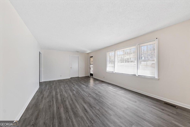 spare room with baseboards, visible vents, dark wood finished floors, and a textured ceiling