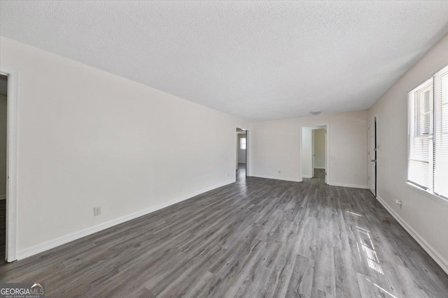 unfurnished living room with a textured ceiling, baseboards, and wood finished floors