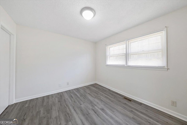 empty room with visible vents, a textured ceiling, baseboards, and wood finished floors