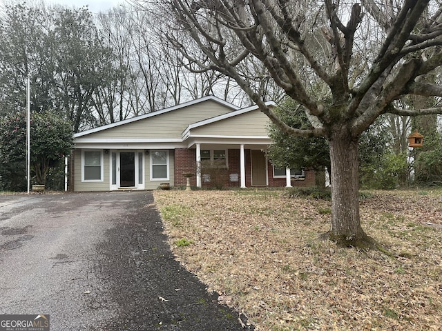 single story home with driveway, brick siding, and a porch