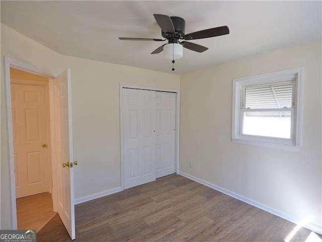 unfurnished bedroom featuring ceiling fan, a closet, baseboards, and wood finished floors