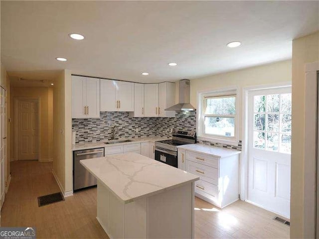 kitchen with white cabinets, wall chimney exhaust hood, appliances with stainless steel finishes, a sink, and backsplash