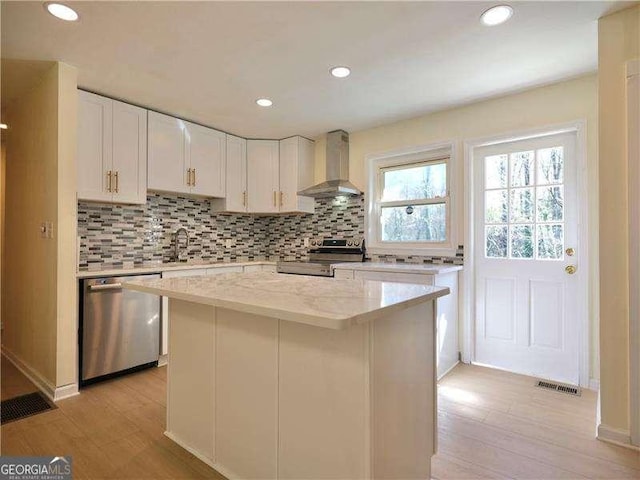 kitchen with stainless steel appliances, wall chimney range hood, light wood-type flooring, and decorative backsplash