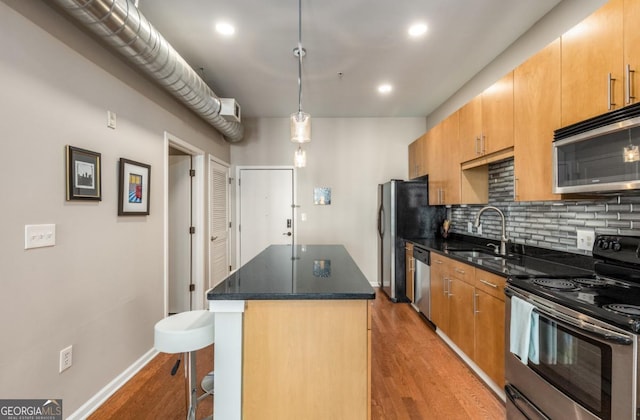 kitchen featuring a sink, a kitchen breakfast bar, appliances with stainless steel finishes, a center island, and tasteful backsplash