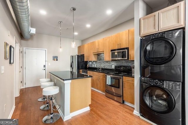 kitchen featuring dark countertops, a kitchen island, a kitchen breakfast bar, stainless steel appliances, and stacked washing maching and dryer