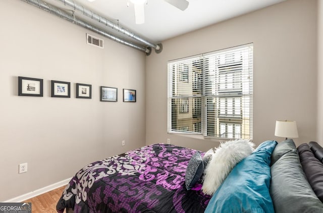 bedroom with a ceiling fan, visible vents, baseboards, and wood finished floors