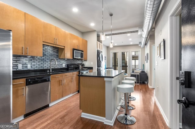 kitchen with appliances with stainless steel finishes, dark countertops, a sink, and a center island