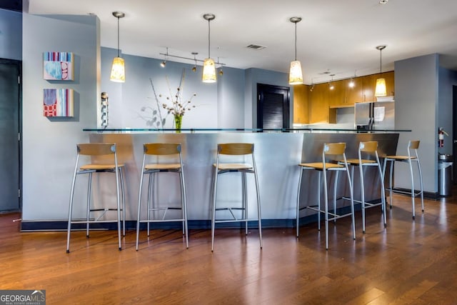 kitchen with wood finished floors, visible vents, a kitchen breakfast bar, stainless steel fridge with ice dispenser, and pendant lighting