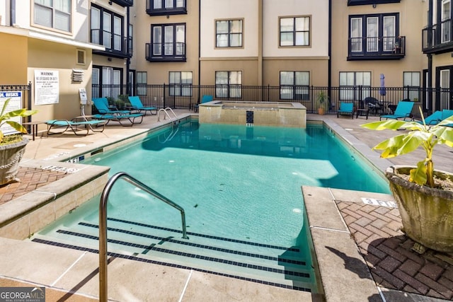 view of swimming pool featuring a pool with connected hot tub, fence, and a patio