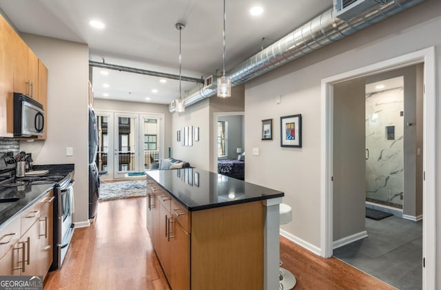 kitchen with wood finished floors, a kitchen island, baseboards, appliances with stainless steel finishes, and decorative light fixtures