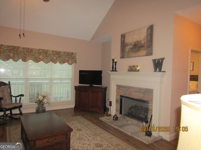 living room featuring high vaulted ceiling, wood finished floors, and a stone fireplace