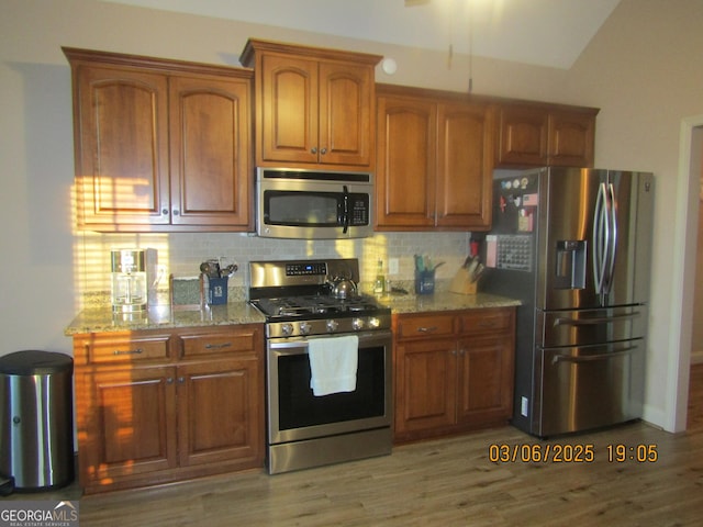 kitchen with appliances with stainless steel finishes, brown cabinetry, light stone counters, and decorative backsplash