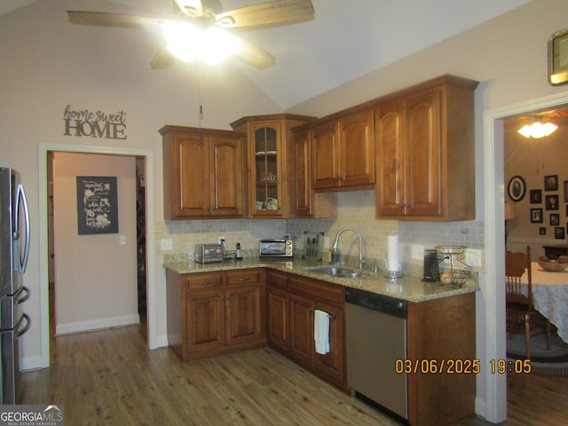 kitchen featuring light stone counters, brown cabinets, a sink, stainless steel appliances, and backsplash