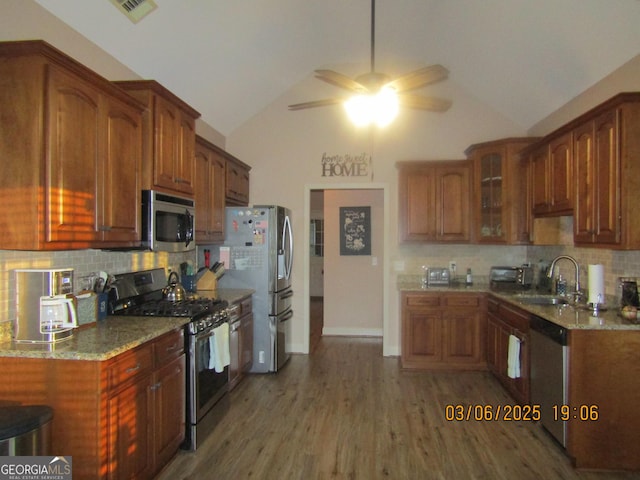 kitchen featuring wood finished floors, a sink, vaulted ceiling, appliances with stainless steel finishes, and glass insert cabinets