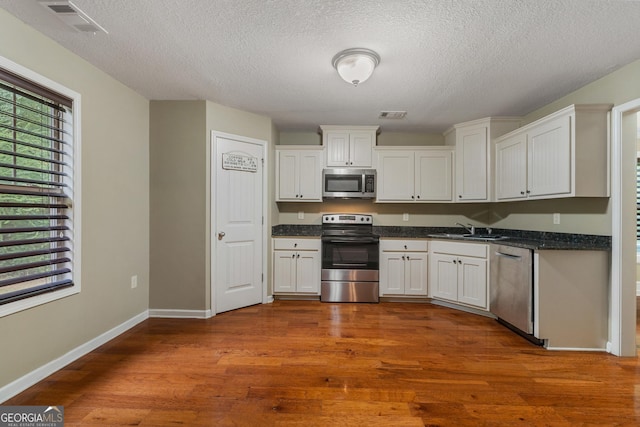 kitchen with stainless steel appliances, dark wood-type flooring, a sink, and visible vents