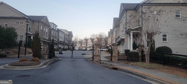 view of road featuring curbs, a residential view, sidewalks, and a gate
