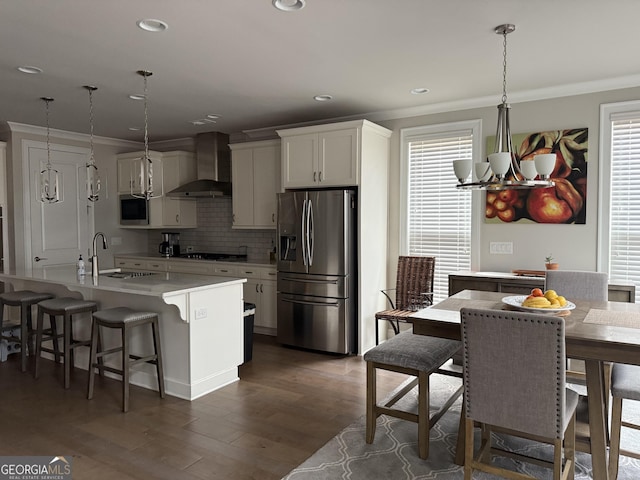 kitchen featuring a sink, stainless steel appliances, crown molding, backsplash, and wall chimney range hood