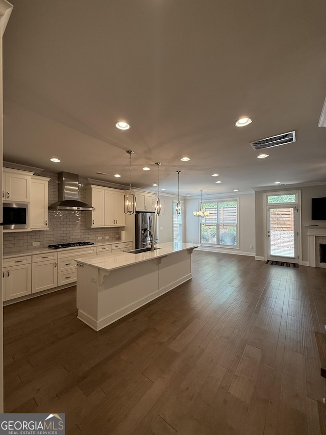 kitchen with visible vents, wall chimney exhaust hood, open floor plan, white cabinets, and appliances with stainless steel finishes