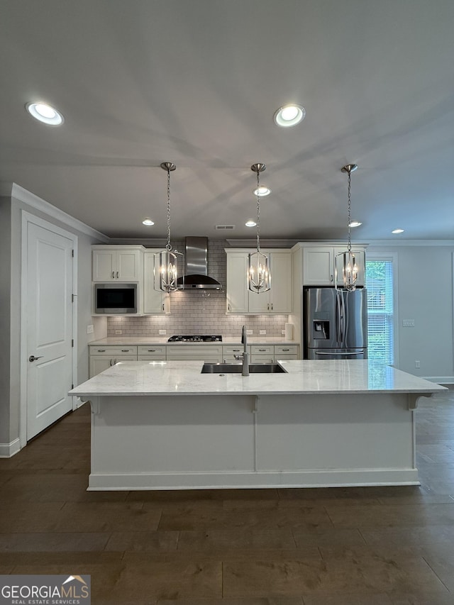 kitchen with a sink, stainless steel appliances, wall chimney range hood, a chandelier, and white cabinetry