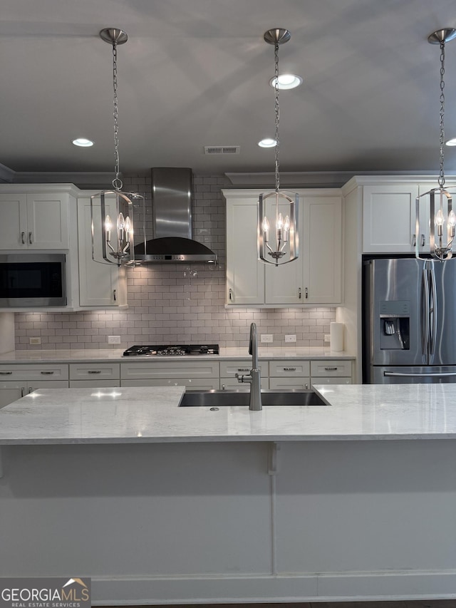 kitchen featuring wall chimney range hood, an inviting chandelier, appliances with stainless steel finishes, and a sink