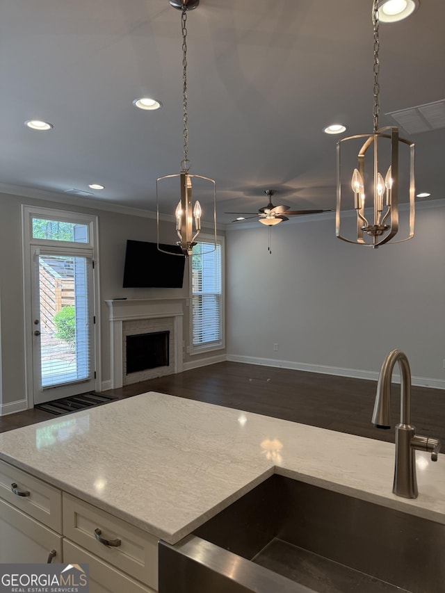kitchen featuring a fireplace, crown molding, a wealth of natural light, and ceiling fan with notable chandelier