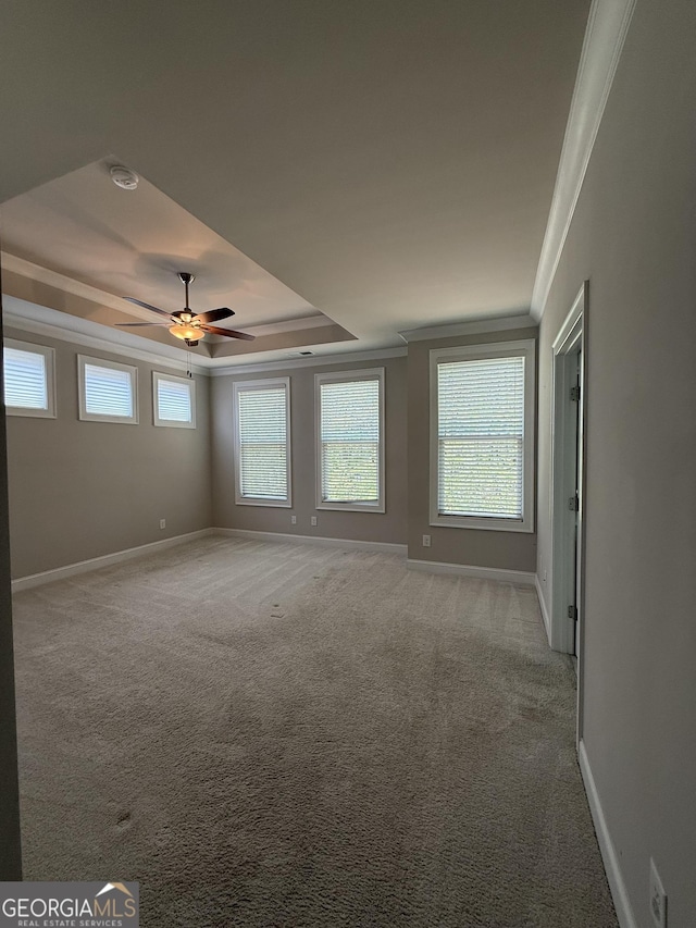 empty room with a ceiling fan, a tray ceiling, baseboards, ornamental molding, and light carpet