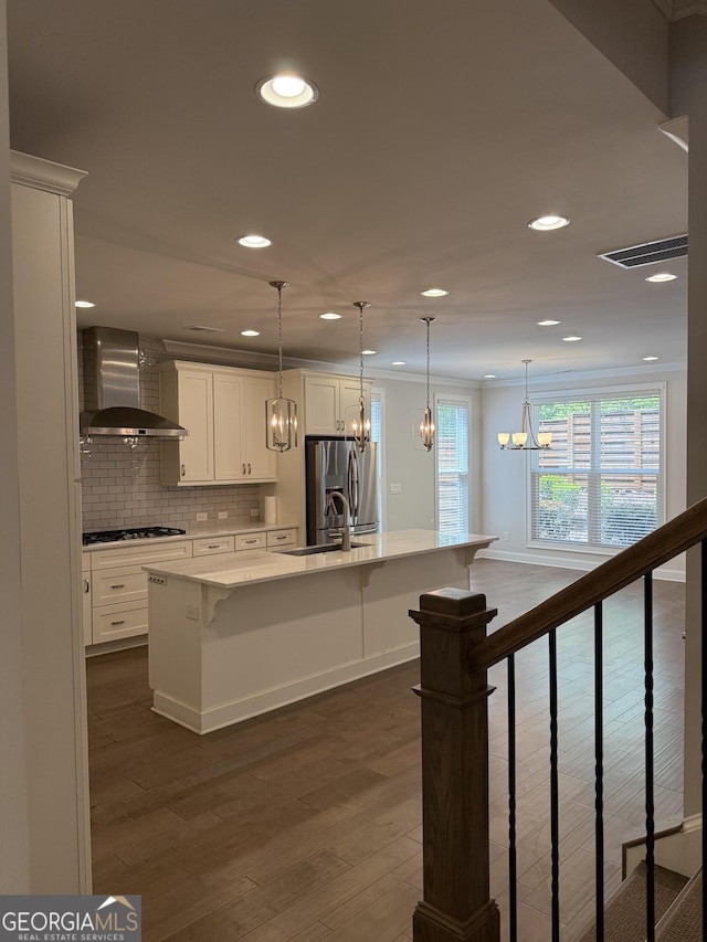 kitchen with a notable chandelier, a kitchen bar, wall chimney range hood, white cabinets, and appliances with stainless steel finishes