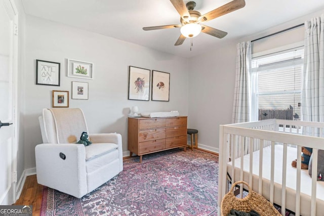 bedroom featuring a nursery area, ceiling fan, wood finished floors, and baseboards