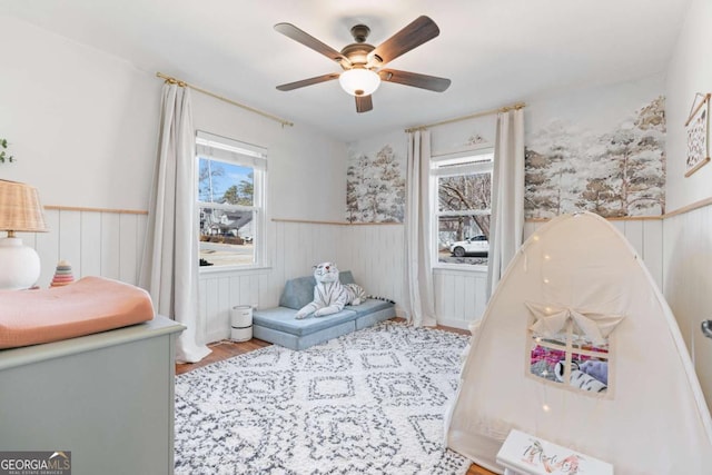 rec room featuring a wainscoted wall, ceiling fan, and wood finished floors