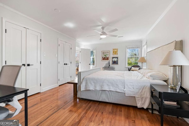 bedroom with ornamental molding, a ceiling fan, two closets, and wood finished floors