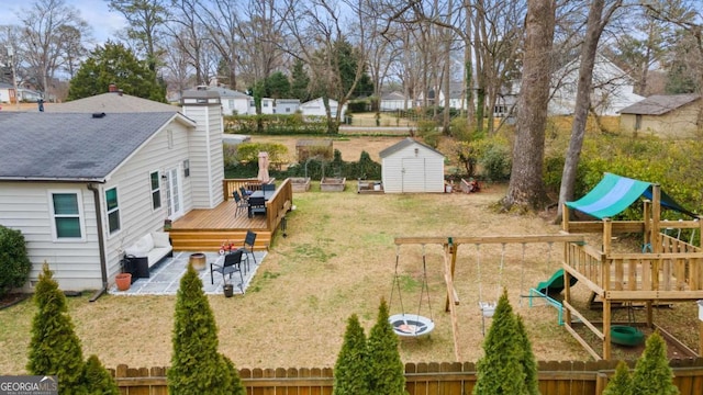 view of yard with an outbuilding, fence, a wooden deck, a shed, and a playground