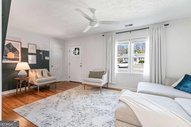 interior space with a textured ceiling, ceiling fan, wood finished floors, visible vents, and baseboards