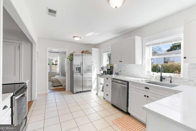 kitchen with light tile patterned floors, stainless steel appliances, a sink, visible vents, and backsplash