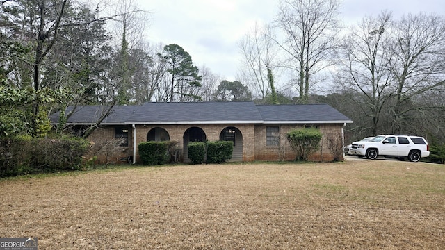 ranch-style house featuring brick siding, a shingled roof, and a front yard