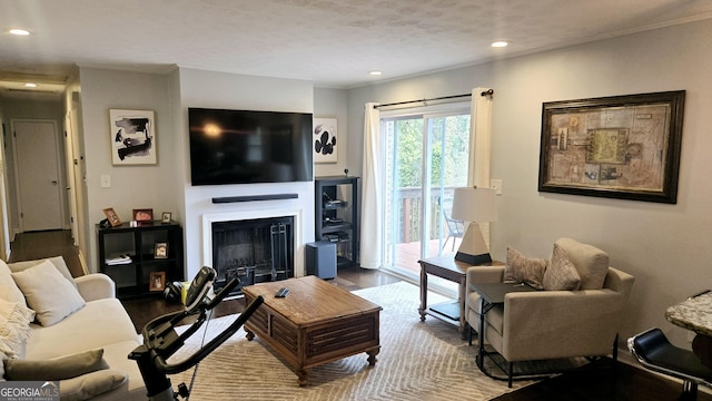 living room with recessed lighting, crown molding, wood finished floors, and a glass covered fireplace