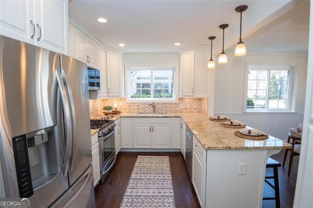 kitchen featuring light stone counters, stainless steel appliances, a peninsula, a sink, and white cabinetry