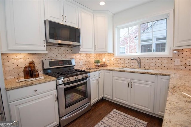 kitchen featuring a sink, white cabinetry, appliances with stainless steel finishes, decorative backsplash, and light stone countertops